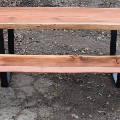 Custom wood slab coffee table with black metal legs displayed on gravel surface, featuring natural grain and knots in warm-toned lumber.