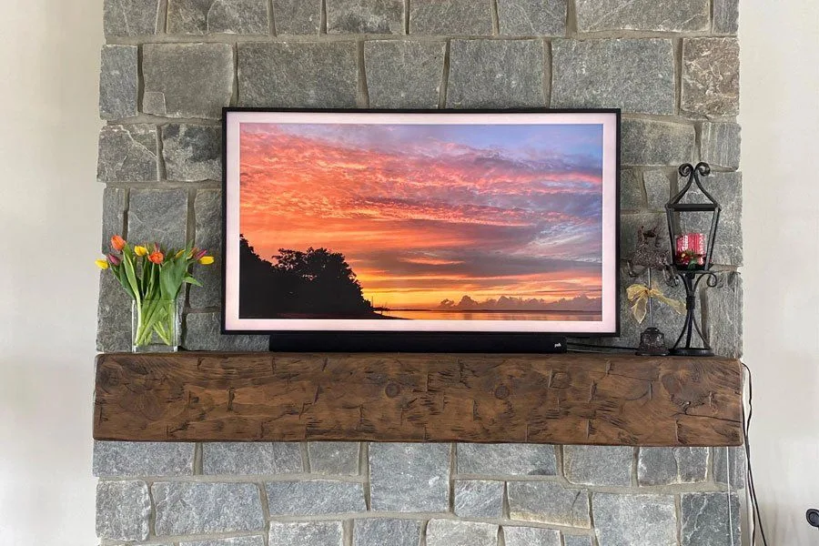 Rustic reclaimed wood mantel mounted on gray stone fireplace surround, displaying a flat-screen TV with decorative accents including fresh tulips and a wrought-iron candle holder.