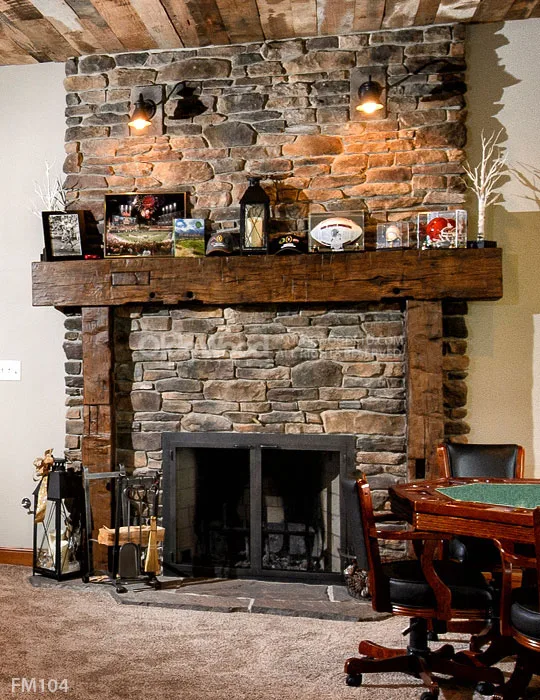 Massive reclaimed wood fireplace mantel with hand-hewn beam construction anchors a stone fireplace, complemented by rustic ceiling beams in a traditional living room.