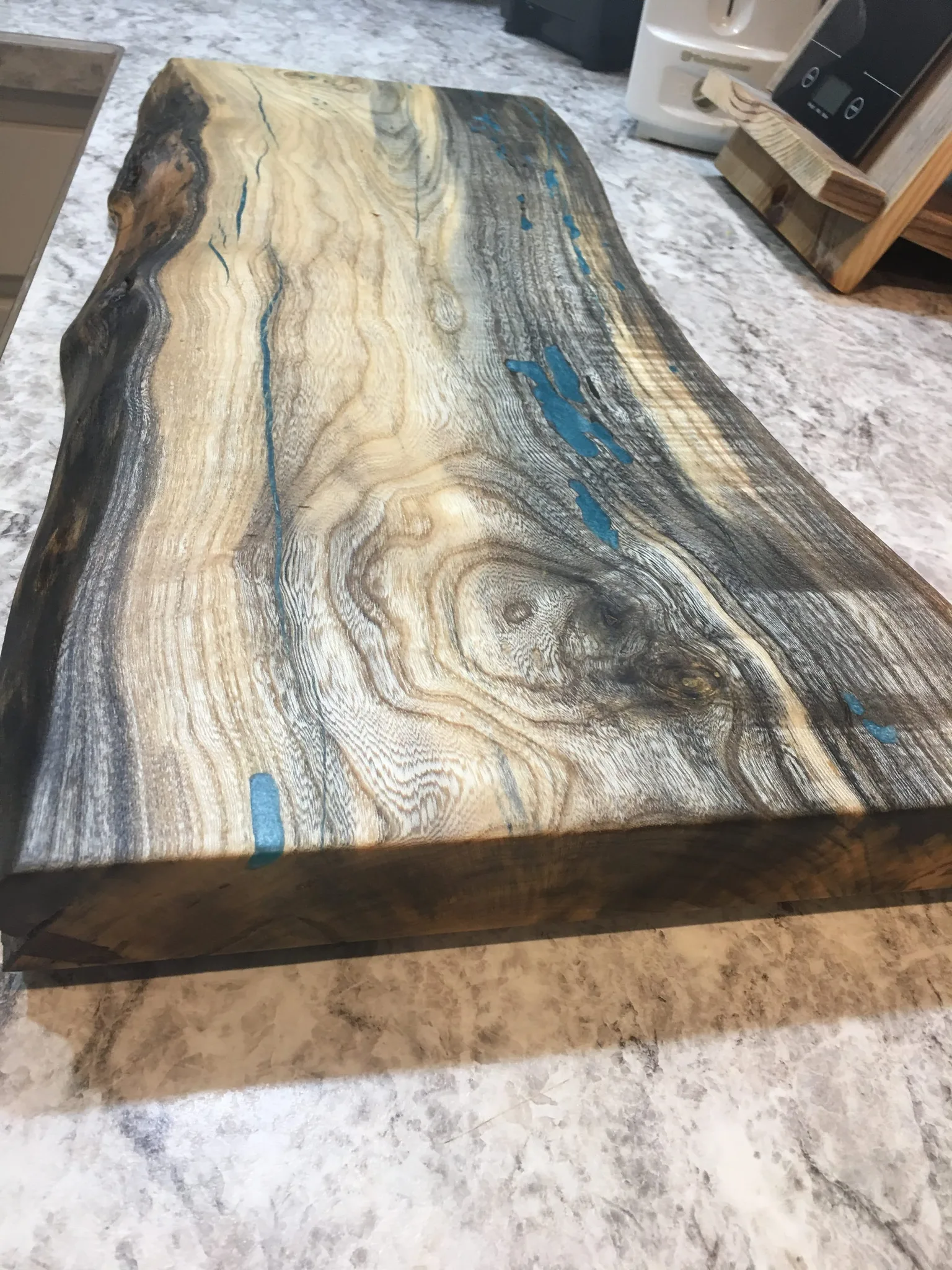 Live-edge wood slab countertop with dramatic natural grain patterns and turquoise epoxy resin inlay accents on marble base.
