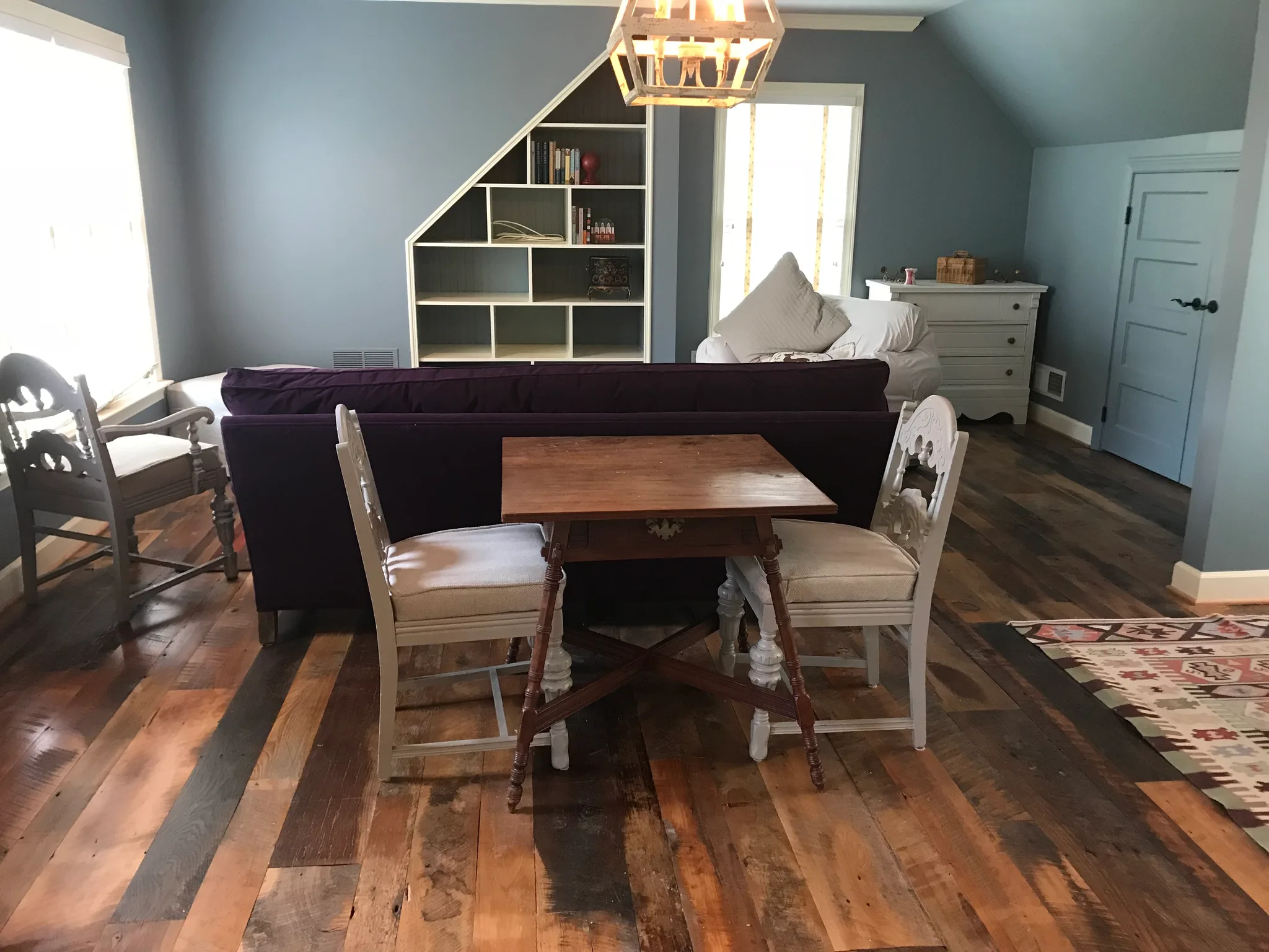 Reclaimed barnwood flooring with varied tones and weathered patina creates rustic character in a multi-functional bedroom space with sloped ceiling.