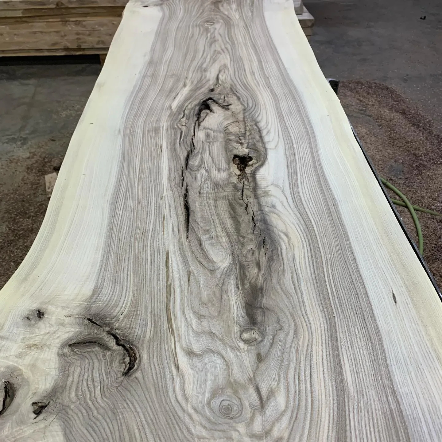 Unfinished live-edge wood slab with dramatic natural grain patterns, knots, and character marks displayed in a lumber showroom.