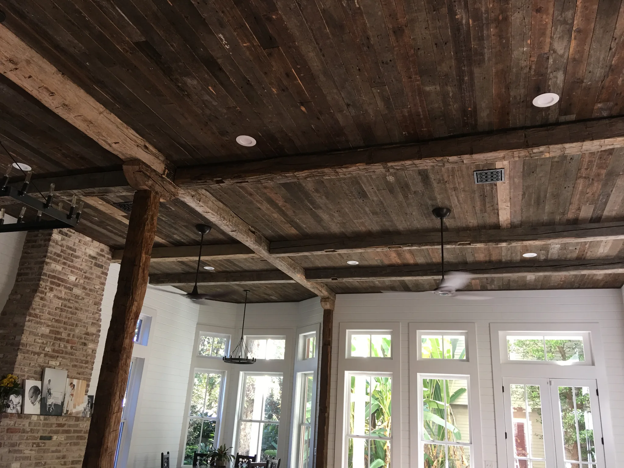 Reclaimed barnwood ceiling planks and exposed structural beams create dramatic rustic character in a bright, modern living space with white shiplap walls.