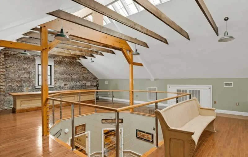 Exposed timber ceiling beams and hardwood flooring create a dramatic vaulted loft space with rustic industrial character and natural light from skylights.
