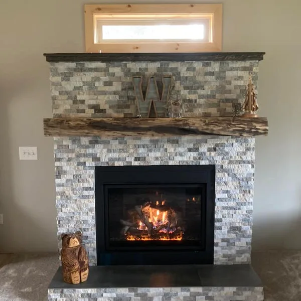 Rustic live-edge wood slab fireplace mantel with natural bark edges mounted above stone tile surround and modern gas insert.