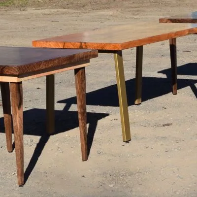 Two custom live-edge wood slab tables with contrasting leg designs displayed outdoors, showcasing figured grain patterns and natural edge details.