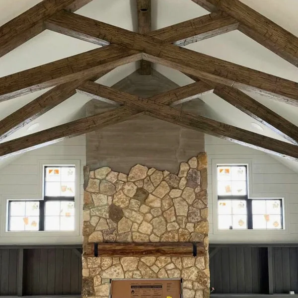 Dramatic vaulted ceiling with exposed reclaimed wood beams in a cathedral-style arrangement above a stone fireplace with rustic wood mantel.