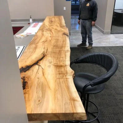 Dramatic live-edge wood slab desk or console table displayed in a modern showroom, featuring natural edge contours and striking grain patterns with dark mineral streaks.