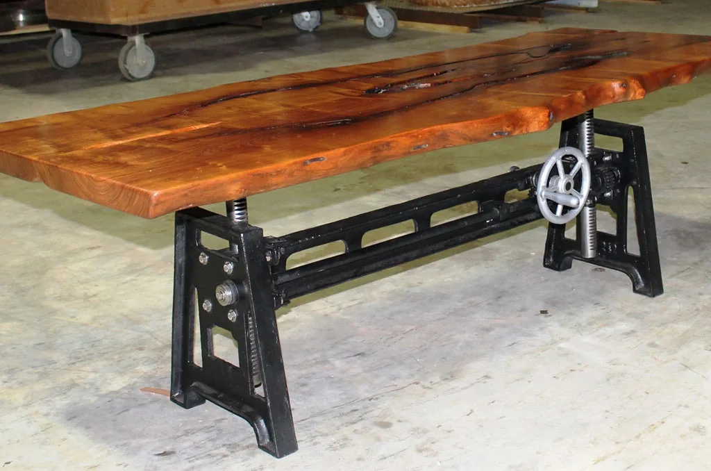 Live-edge wood slab table with industrial black metal crank base featuring adjustable height mechanism and natural edge detail.