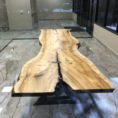 Dramatic live-edge wood slab dining table with black epoxy river inlay on modern metal base in contemporary showroom setting.